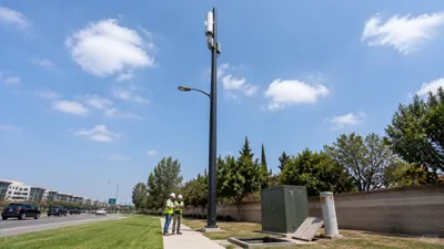 Ground-level engineers reviewing plans beneath a 5G small cell mounted high on a streetlight pole
